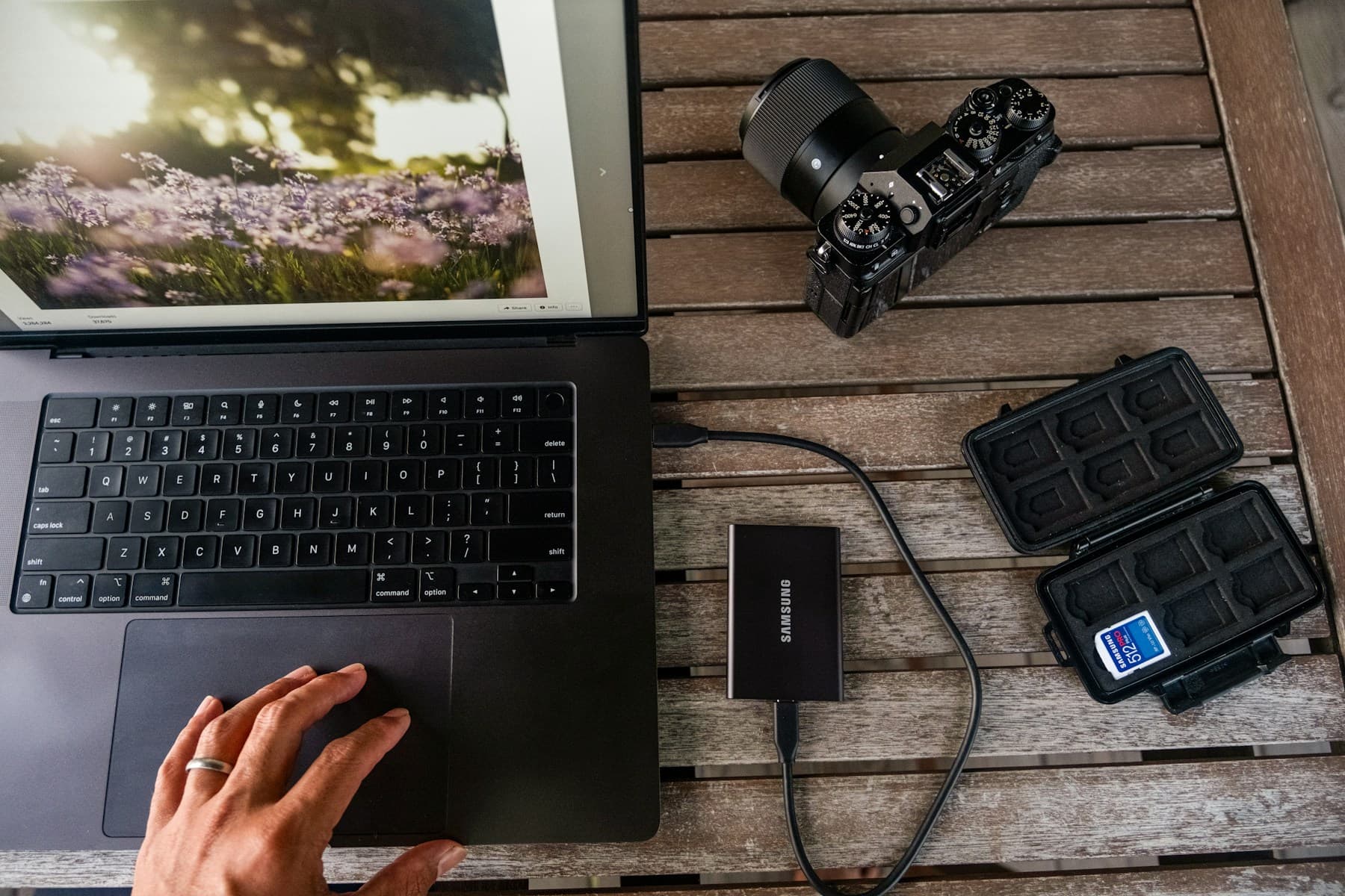 A laptop, camera, memory card reader, and SD card on a wooden table