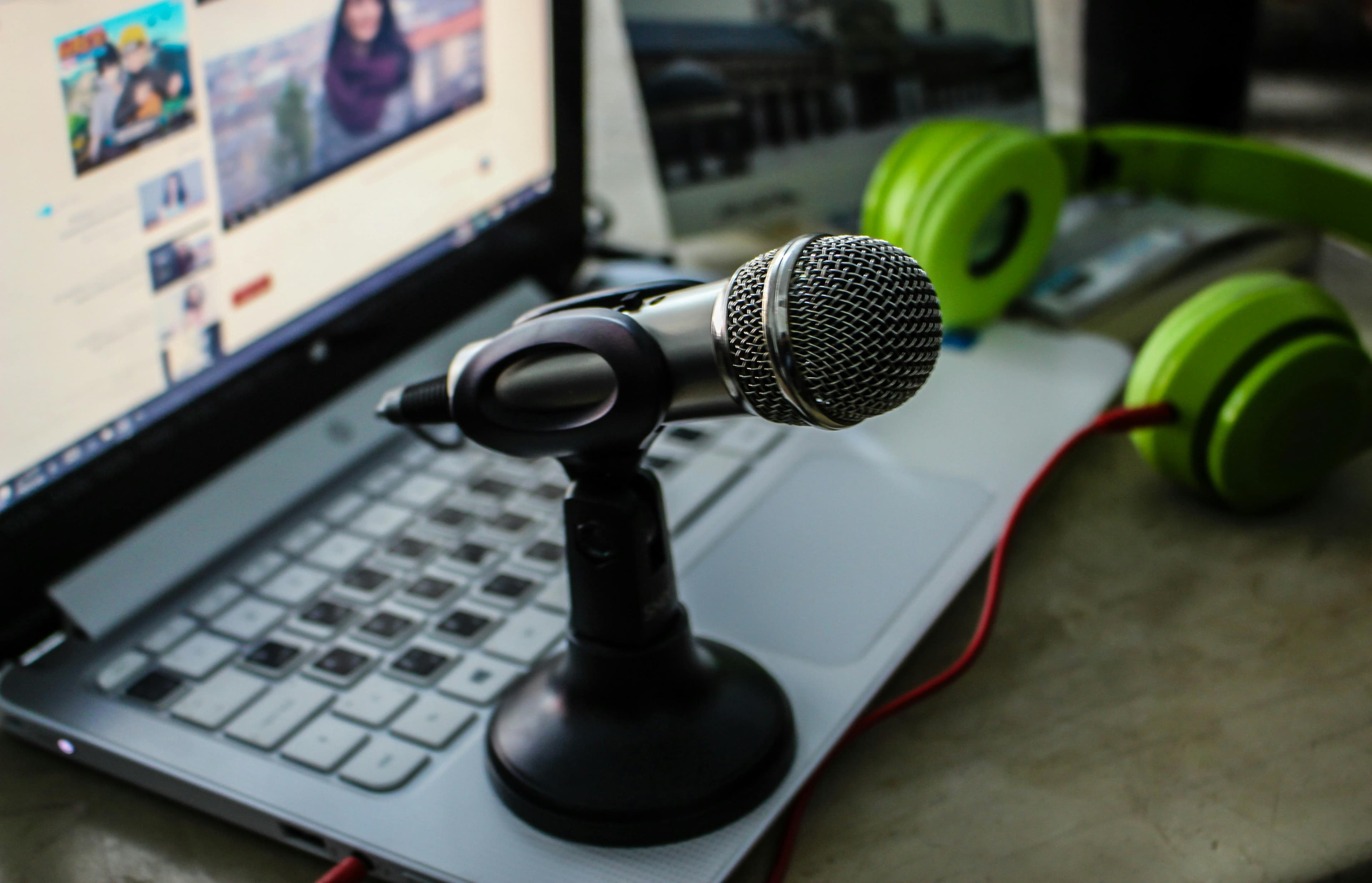 A microphone on a laptop beside green headphones